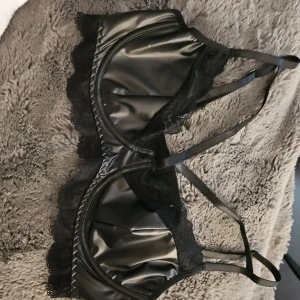 Svart bh "skinnimitation " - Oanvänd Snygg bh med spetsdetaljer och korsade band. Perfekt för en festlig kväll . Lappen är borttagen men passar en b kupa. Katt finns I hemmet