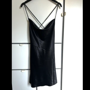 Satinklänning med öppen rygg  - En kort satinkläning med lägre rygg där banden är korsade, helt oanvänd med prislappen kvar