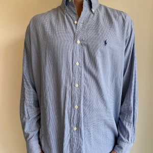 Ralph Lauren skjorta  - Blå Ralph Lauren skjorta i storlek M. Skjortan är i fint skick utan några skavanker. Den är något bred i storleken. Har en liten fläck på baksida axel. Modellen är 186 cm lång. Orginalpris ca 1500 kr och nu endast 499. 
