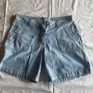 Ljusblå jeansshorts från Fresh Spirit - Ett par ljusblå jeansshorts från Fresh Spirit med en knapp och dragkedja framtill. Shortsen har två framfickor och två bakfickor samt hällor för bälte.