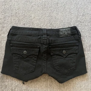 Svarta jeansshorts från True Religion - Midjemått är 36,5 cm raktöver och längden på shortsen är 30cm 🩷 Svarta jeansshorts från True Religion med klassisk femficksdesign och knappgylf. Shortsen har en rå kant vid bensluten och dekorativa sömmar på bakfickorna.
