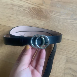 Svart bälte med gulddetalj från HM - Ett svart bälte med gulddetalj i form av två ringar fram från HM. Storleken är S. Det har gjorts tre extra hål (som går att se på bild 3) Bältet är i bra skick. 