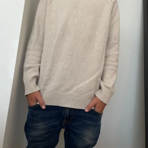 Beige stickad tröja - En enkel och bekväm beige stickad tröja med långa ärmar och ribbstickade muddar vid ärmslut och nederkant. Tröjan har en normal passform och är perfekt för höst- och vintersäsongen.