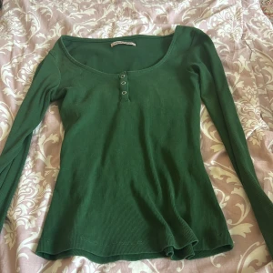 Grön ribbad tröja från Anna Field - En grön ribbad tröja från Anna Field med rund halsringning och tre knappar framtill. Tröjan har långa ärmar och en figurnära passform.