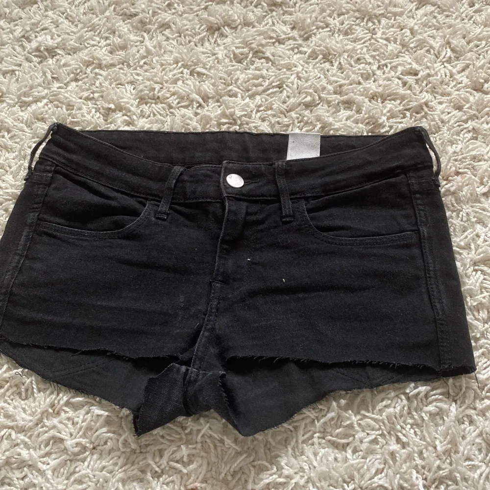 Ett par svarta jeansshorts från H&M med låg midja. Shortsen har en skinny passform och de har en rå kant vid benen och klassiska fyra fickor.. Shorts.