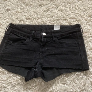 Svarta jeansshorts från H&M - Ett par svarta jeansshorts från H&M med låg midja. Shortsen har en skinny passform och de har en rå kant vid benen och klassiska fyra fickor.
