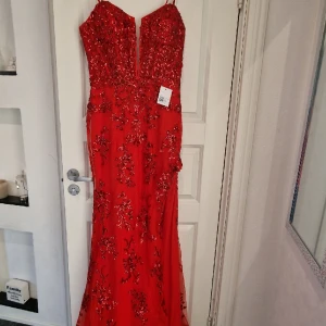Röd balklänning - Säljer denna fina röda balklänning då den är lite för liten och har hittat en annan.   Aldrig använd bara testad.   Paljetter i mönster på hela klänningen, storlek 42 men snörning i ryggen så den går att justera lite.