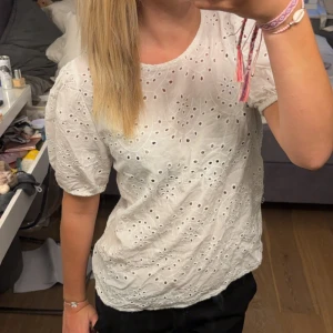 Vit blus från Jacqueline de Yong - En vit blus från Jacqueline de Yong med broderade detaljer och hålmönster. Blusen har korta puffärmar och en knapp i nacken. bra skick men inte super. Därför säljer jag den billigt.💕