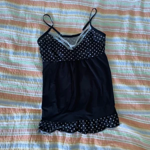 Svart prickig linnetopp med spets - En svart linnetopp med vita prickar och spetsdetaljer. Toppen har smala axelband och en volangkant längst ner.