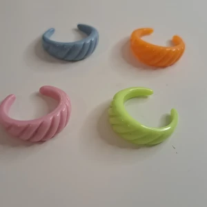 Färgglada ringar i plast - Fyra färgglada ringar i plast med en vriden design. Ringarna finns i färgerna blå, orange, rosa och grön.