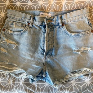 Ljusa jeansshorts från Zara - Ljusa jeansshorts från Zara med slitna detaljer och fransiga kanter. Shortsen har en knappgylf.