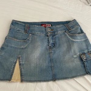 Jeanskjol - En kort jeanskjol coola detaljer. Kjolen har en dragkedja och knapp framtill samt en liten slits på framsidan. Midjemåttet rakt över är ca 43,5 cm och längden från midjan till grenen är ca 32,5cm. Använd gärna köp nu💕