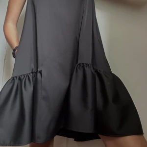 Svart volang klänning  - Otrolig klänning med lätt glansigt tyg. I gott skick. Har fickor! Räcker ner till precis över knäna på mig som är 170cm. 