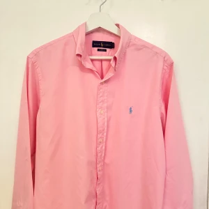 Ralph Lauren skjorta - Tjena! Säljer denna fräscha skjorta i färgen rosa i mycket bra skick, den är nytvättad och nystryckt. Dessa är perfekt i vilken garderob som helst oavsett om man vill ha en klassisk look för jobbet eller en avslappnad stil för vardagen👔