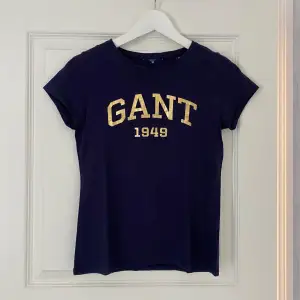 Marinblå t-shirt med guldig text från GANT i storlek XS. Sparsamt använd så i väldigt fint skick!💙