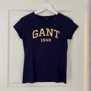 GANT t-shirt  - Marinblå t-shirt med guldig text från GANT i storlek XS. Sparsamt använd så i väldigt fint skick!💙