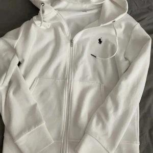Polo Ralph Lauren Zip Hoodie - En vit polo ralph lauren zip hoodie i bra skick. Den är använd men har fortfarande mycket kvar att ge. Storleken är S. Hör av er vid eventuella frågor! 🤝