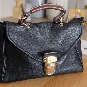 Mulberry Polly Push Lock satchel läder, stl: 34x24x11cm  - Modell: Mulberry Polly Push Lock satchel  The vintage-inspired Mulberry Polly Push Lock bag features a pebbled leather exterior and has a contrast brown leather top handle and detachable cross-body strap. It features a statement push lock fastener on