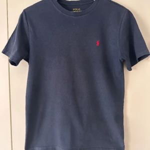 Ralph lauren t shirt - Säljer denna fina blå t-shirt ifrån ralph lauren. Skulle säga att skicket på tröjan var 8/10 och storleken på tröjan är 10-12 ( m ) Junior men passar dig som ör 13-14 också. Nypris 595 kr mitt pris 199 , hör av er vid fler frågor och bilder.