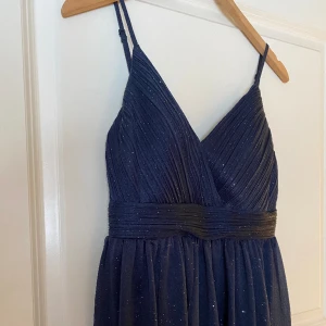 Balklänning  - Mörkblå balklänning Klassisk långklänning med glittrigt tyg från Helena Granby Design. Använd en gång. Transparent kjoltyg med kortade underkjol. Vadderade kupor.  Passar mig som är 175 cm lång och bär stl M. Kjolen kan läggas upp. Fler bilder finns 