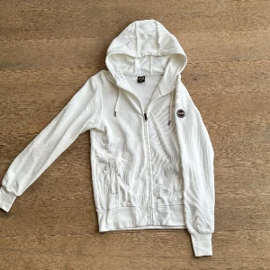 Vit Colmar full-zip med huva - Skick: Mycket bra (Oanvänd) Material: Bomull  Storlek: Står S men passar även till M (Killen på bilden är M) 