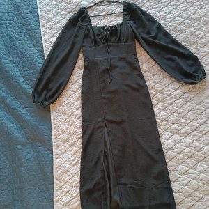 Svart klänning i storlek XS!  - Svart klänning i storlek XS från Gina Tricot! Klänningen är helt ny, har ej använts! Klänningen har en slits framtill och knytning vid bröstkorgen. Det är en långärmad klänning med puffärm med en fyrkantig urringning fram och baktill. 