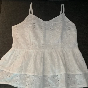 Vitt linne, top med brodyr  - Vitt linne/topp med fin volang och brodyr. Reglerbara axelband. Dragkedja i sidan.