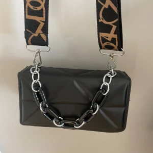 axelremsväska  - väska med justerbart band och en kedja på