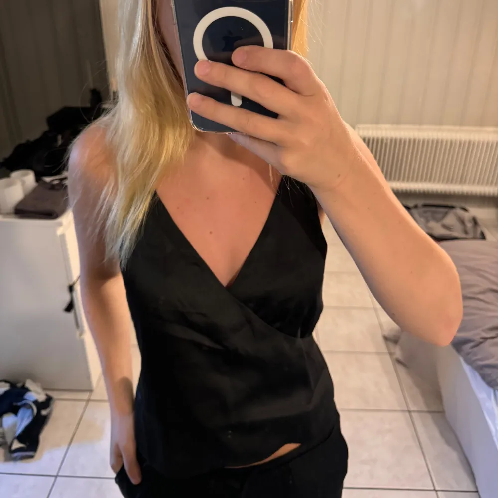 En elegant svart V-ringad satin singlet från NA-KD. Toppen har smala axelband och en figurnära passform, perfekt för festliga tillfällen.. Yläosat.
