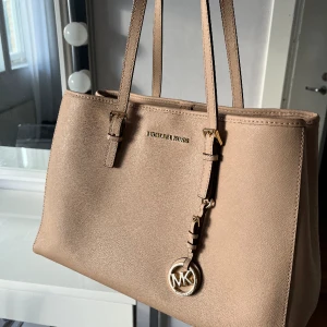 Michael Kors väska - Säljer den här fina beiga väskan från Michael kors. Den är i använt skick, men inte trasig på något sätt, bara några fläckar på undersidan och tappat lite av sin stadga. 