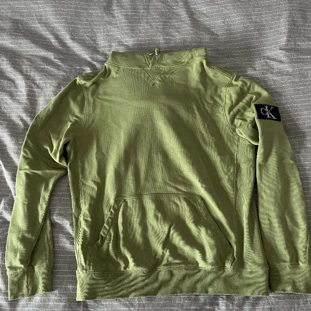 Ljusgrön Calvin Klein Hoodie med fastsydd patch med logga på ärmen. En aning oversized.  Nypris: 1099kr  Skick: Bra, använd några gånger, inga synliga brister  Säljs för att den inte passar mig. Hoodies.
