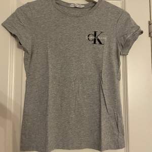En grå Calvin Klein T-shirt med svart/vit märke. Använd få tal gånger. Storlek för 12-åringar, passar mig som en ganska smal o bär xss/xs.