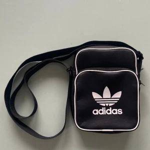 Svart Adidasväska.  - Svart adidasväska i prima skick. 21x17 cm. Reglerbart axelband (4 cm brett) 