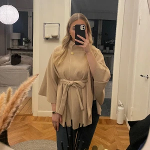Poncho  - Beige mjuk poncho med guldknapp. Justerbart skärp i midjan så passar de flesta. Aldrig använd. Lappar kvar. 
