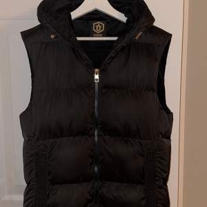 En svart Glorious Gangsta Alfrez Gilet Dunväst som inte säljs längre. Köpt på Zalando för 656kr, digitalt bevis finns om så önskas. Inga hål eller fläckar. Passar mig bra som är ca 190cm och väger ca 70kg. Storlek M men är större i storleken.