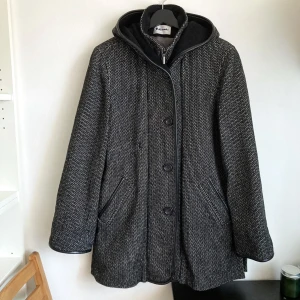 Hettemarks kort ull kappa med huva, 40 M, svart & vit, vinter, vintage, retro - Ullkappa från Hettemarks. Stängning med dragkedja och knappar, hög krage, slitsar i sidorna, öppna sidfickor, två innerfickor med knapp. Lagning på bröstet och slitning på fodret. Mått i cm: bröstvidd 57; axelbredd 45; längd från axeln 83; ärm 66.