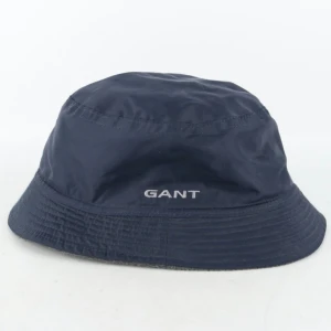 Gant Bucket Hat till ca 9/10 åring  - Varumärke: Gant Produkt: Bucket hat/Fiskehatt Färg: Mörkblå Storlek: L (9-10 years, 134-140 cm) Material: 100% Nylon, foder tunn fleece   Skick: Har använts fåtal ggr, i fint skick, inget särskilt att anmärka på.