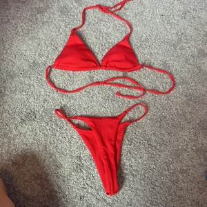 Röd bikini - En röd bikini med triangelöverdel och knytband. Underdelen har smala sidoband.