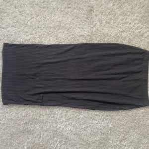 Grå långkjol - Säljer en lång, grå kjol med ribbstickade detaljer och en slits på baksidan. Mycket bra skick då den använts enbart en gång Kommer längre inte till användning, därav säljs den