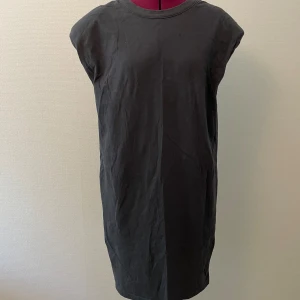 Svart klänning med axelvaddar - Svart klänning med tryck på baksidan av märket Cheap Monday. Rund halsringning och korta ärmar med axelvaddar (går att ta ur).