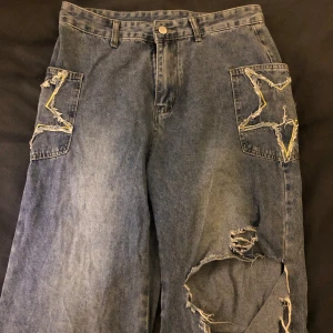 Byxor L med stjärnor - Storlek large, Lite Y2K såkallade ”mamma jeans”. Med hål på knäna, en hyfsat lång riva är i hålet som jag tidigare försökt sy ihop med mina limited skills, (lätt att fixa om man kan sy). Står tyvärr inget märke på dom.
