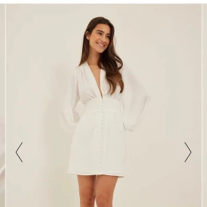 Vit satin studentklänning - Vit satin nakd miniklänning med ryggdragkedja, v-ringad, knappar framtill & går till knäna.😍 True to size/liten i stl.  Aldrig använd & prislapp kvar. Gammal modell så finns ej kvar att köpa! Ordinariepris 599kr.  Hör av dig innan du trycker på köp🥰