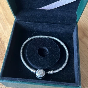 Pandora armband med guld detaljer storlek 17 - Pandora armband, använd bara ett par gånger. Den har guld detaljer pa själva knäppet och stenar i mitten, vilket innebär att den är passande för guld och silver.