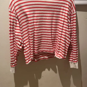 En röd randig zarattröja - En randig långärmad tröja som är lite kortare men inte en magtröja, den är inte så använd och kommer inte till användning 