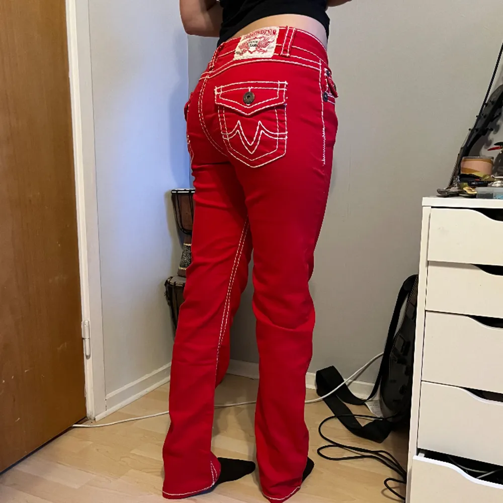 Röda True religon liknande byxor med vita sömar & detaljer längst med byxorna och på fickorna  Midjemått rakt över= 40cm Innerbenslängd= 75cm Längd på hela= 103cm . Jeans & Byxor.