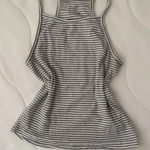 Randig linnetopp från H&M - Säljer en vit och svart randig linnetopp från H&M Basic i ekologisk bomull. Toppen har smala axelband och tajt passform. Perfekt för varma dagar och enkel att matcha med jeans eller shorts.