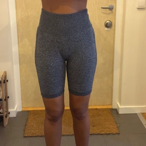 Grå högmidjade cykelshorts - Säljer ett par gråmelerade cykelshorts med hög midja och tight passform. De är stretchiga och perfekta för träning eller chill. Materialet är mjukt och följsamt, vilket gör dem riktigt bekväma att ha på sig. Snygga och enkla att matcha med en sportig look.