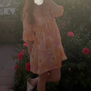 Sommarklänning blommönster - Supersöt kortklänning med blommigt mönster i ljusa toner av rosa, orange och gul. Trevartsärmad och luftigt material. Passar Xs och S klänningen är i nyskick.