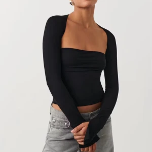 Svart croppad bolerotopp med långa ärmar - Säljer en svart, croppad bolerotopp med långa ärmar och axelbandslös design. Toppen har en tight passform och är tillverkad i ett stretchigt material som sitter snyggt mot kroppen. Perfekt för dig som gillar minimalistisk och trendig stil.