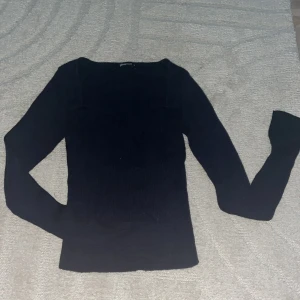 Svart ribbad långärmad topp Gina Tricot - Säljer en svart ribbad långärmad topp från Gina Tricot. Tröjan har en snygg fyrkantig ringning och är figurnära i modellen. Perfekt att styla med jeans eller kjol för en clean look. Materialet är stretchigt och bekvämt.
